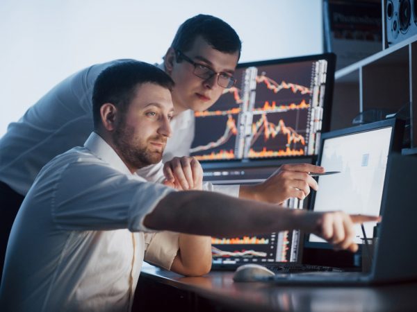 team-of-stockbrokers-are-having-conversation-in-dark-office-with-display-screens-analyzing-data-graphs-and-reports-for-investment-purposes-creative-teamwork-traders (1)